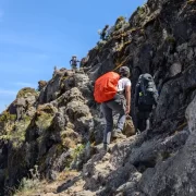Hikers with backpacks ascending a rocky mountain trail on Mount Kilimanjaro, Tanzania.